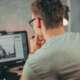 A man with glasses focused on editing a photo on his desktop computer in an office.